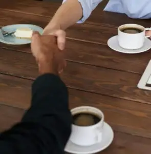 Smiling woman with red hair shakes hands across a table during a coffee meeting.