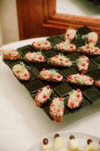Delicious gourmet canapés with toppings served on a stylish black ceramic tray, perfect for appetizers.